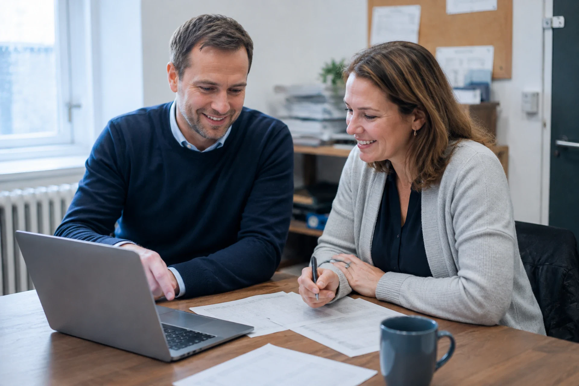 To personer diskuterer finansielle planer ved et bord med laptop og papirer.