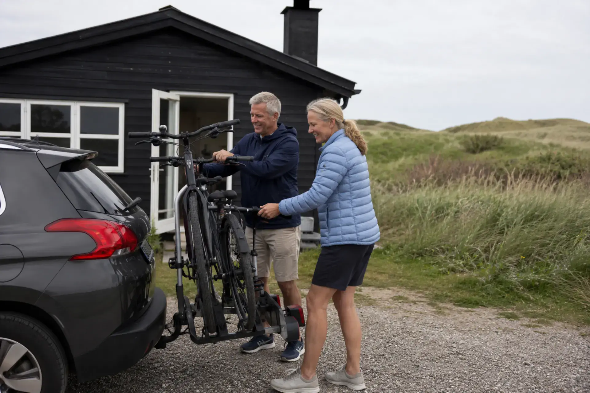 Par, der pakker cykler ud af bil foran en hytte i naturen.